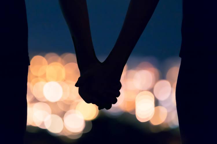 couple holding hands with blurry view of city lights in the distance 