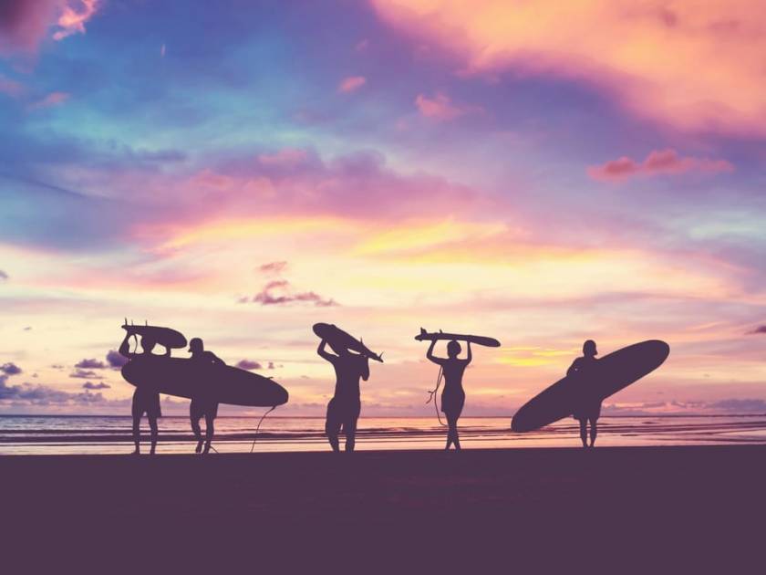 surfers heading to water at sunset